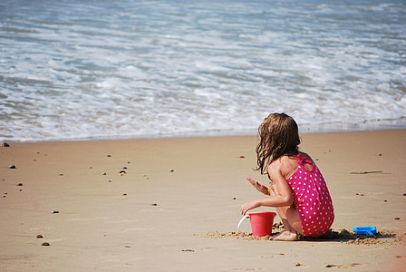 girl in pink and white polka-dot sleeveless onepiece playing on shoreline beside sea thumbnail