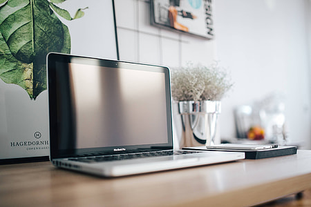 Silver Acer laptop on a wooden desk with a green plant, pencils and an Apple iPhone thumbnail