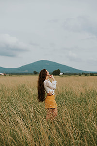 woman in the middle of green and brown wheat plant under gray clouds photo thumbnail