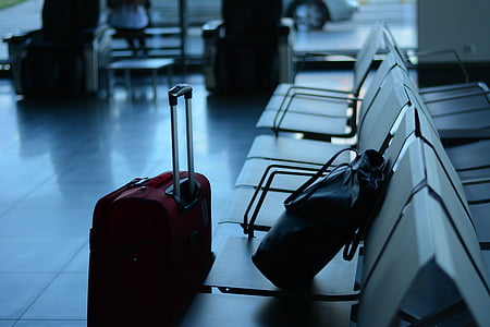 black bucket bag on white gang chair beside maroon luggage on floor inside room thumbnail