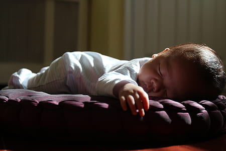baby wearing white footie pajama lying on brown pillow thumbnail