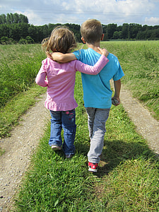 girl and boy walking on grass field pathway thumbnail