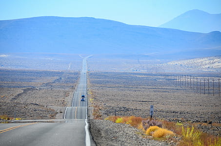 two vehicles running on road surrounded with grass fields thumbnail