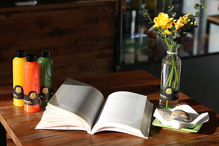 open book on top of table beside flower vase with yellow roses thumbnail