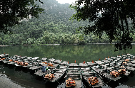 person wearing cone hat sitting on boat between empty boats thumbnail