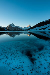 body of water near snow-covered mountain during daytime thumbnail