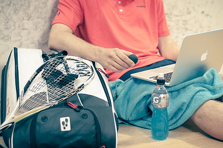 man sitting on beige floor facing opened MacBook near tennis gear thumbnail