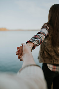 woman facing body of water while holding person's hand thumbnail