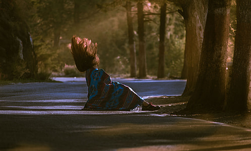 woman sitting on road surrounded by trees thumbnail