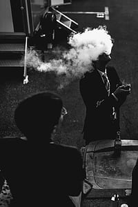 grayscale photography of man smoking beside board with bottle thumbnail