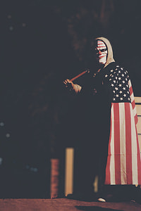 person wearing black, white, and red U.S.A. flag holding brown bat while standing at nighttime thumbnail