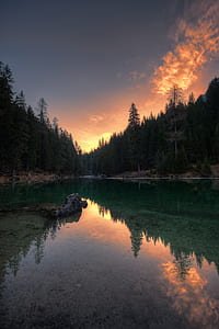 calm river in middle of forest under orange and gray sky thumbnail