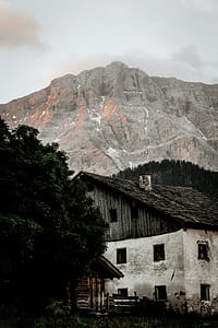 white and black wooden house near gray mountain under gray sky during daytime photography thumbnail