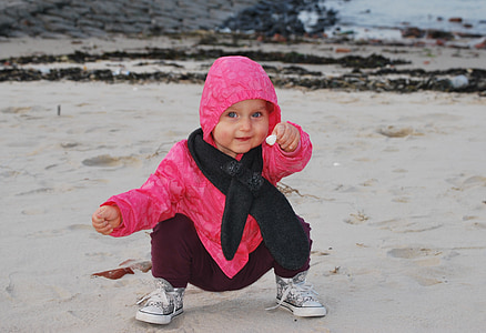 girl squats on grey sand holding flower thumbnail