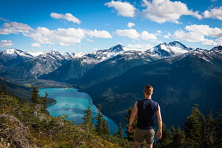 man standing on top of mountain facing on lake during daytime thumbnail