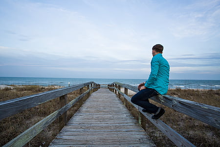 man sitting on dock pathway railing facing sea at daytime thumbnail