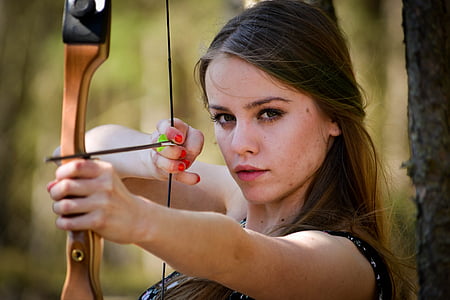 selective focus photography of woman in black top aiming her bow thumbnail