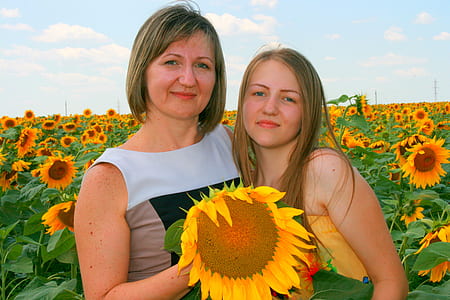 two women standing in sunflower field during daytime thumbnail