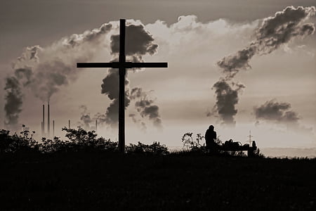 silhouette of person sitting on bench near large cross thumbnail