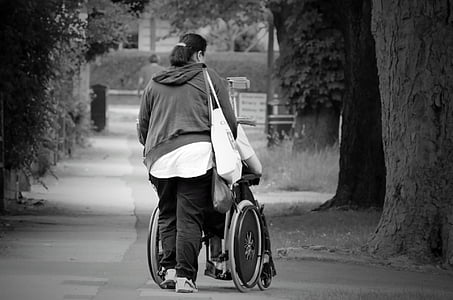 grayscale photography of woman pushing wheelchair thumbnail