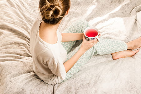 woman holding white cup sitting on bed thumbnail