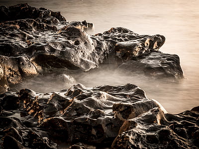 brown and beige rocks on body of water with steam thumbnail