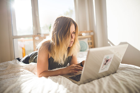 woman on bed while using gray laptop computer thumbnail