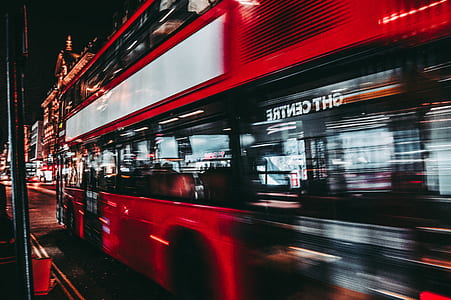 timelapse photography of red double decker bus passing between buildings thumbnail