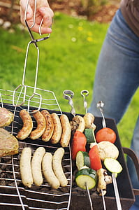person holding grilling sausage and vegetable skewers outdoor thumbnail