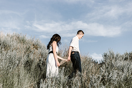 man and woman holding hands while walking on grass field at day time thumbnail