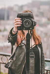 woman standing beside fence holding camera thumbnail