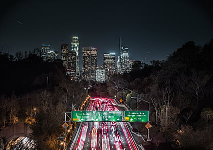 timelapse photo of vehicles on street with green road signs facing high-rise and mid-rise buildings during night time thumbnail