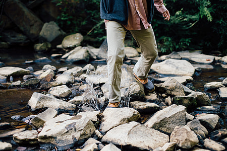 person on brown denim jeans walking on rocky river at daytime thumbnail