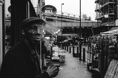 man smoking cigarette standing on sidewalk thumbnail