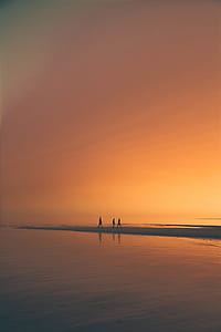 three person walking in the sand beside the beach during sunset thumbnail