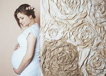 pregnant woman holding her tummy and leaning on brown wall thumbnail