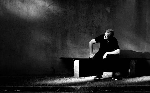 man wearing black shirt and black pants sitting on bench near wall thumbnail