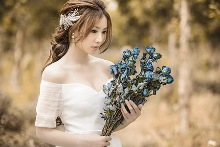 woman in white cold-shoulder dress holding blue flower bouquet thumbnail