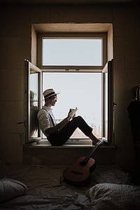 man reading book while sitting on window thumbnail