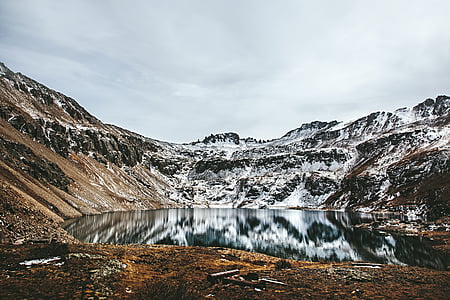 landscape photography of mountain near body of water under white sky thumbnail