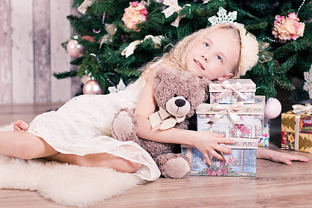 child lying on floor near christmas tree hugging teddy bear and gift boxes thumbnail