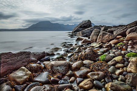 stones on seashore near mountains under cloudy sky during daytime thumbnail