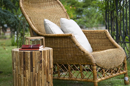 brown wicker armchair and two white throw pillows near brown leather covered book on cut log side table thumbnail
