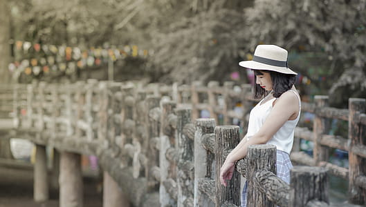 Woman Wearing White Tank Top and White Hat Standing on a Boardwalk thumbnail