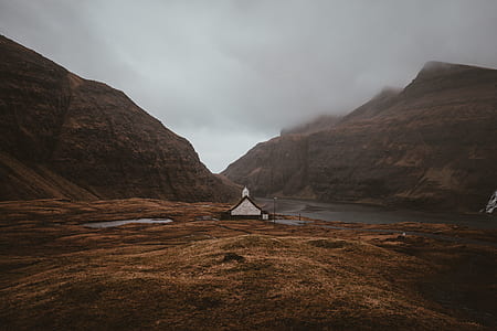 black and white wooden house in the middle of mountains under cloudy sky thumbnail