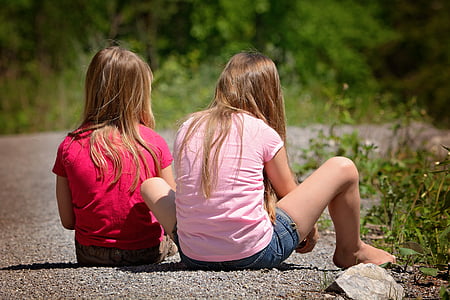 two blonde haired girls sitting on pebbled surface thumbnail