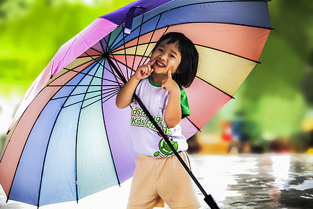 girl in white and green crew-neck t-shirt and brown shorts outfit smiling and holding multicolored umbrella thumbnail