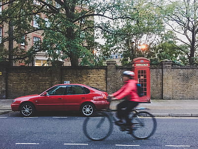 person cycling near red sedan parked on the street thumbnail