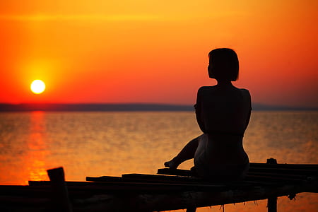 Silhouette of Woman Sitting on Dock during Sunset thumbnail