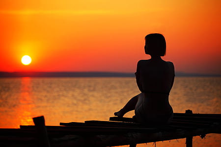 silhouette of woman sitting on dock during golden hour thumbnail